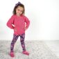 Child in pink sweater and floral leggings smiling.