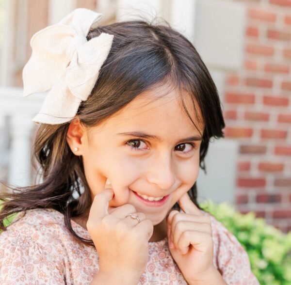 cherished moments kids 14k gold clear cz earrings Smiling girl with bow in her hair outdoors.