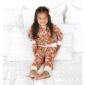 Child in floral pajamas on bed smiling.