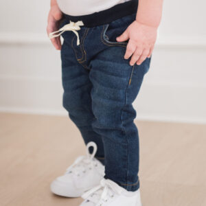 Toddler in jeans and sneakers standing indoors.