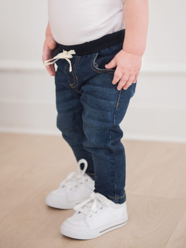 Toddler in jeans and sneakers standing indoors.