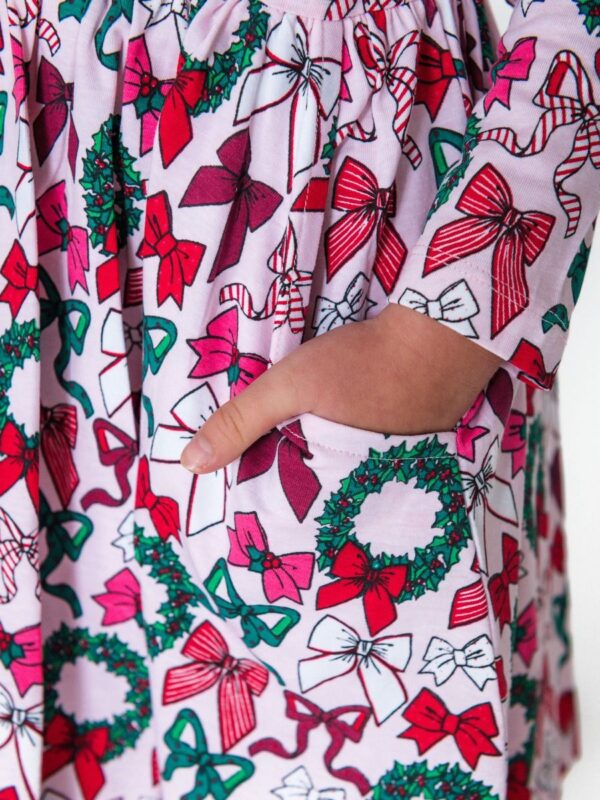 rufflebutts holly bow long sleeve knit twirl dress Child's hand in Christmas-themed dress pocket with bows.