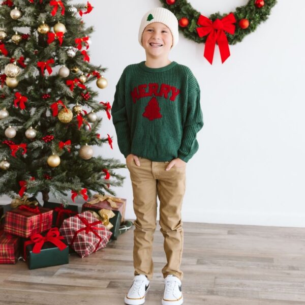 sweet wink merry patch christmas knit sweater Smiling child in Christmas sweater by decorated tree.