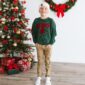 Smiling child in Christmas sweater by decorated tree.