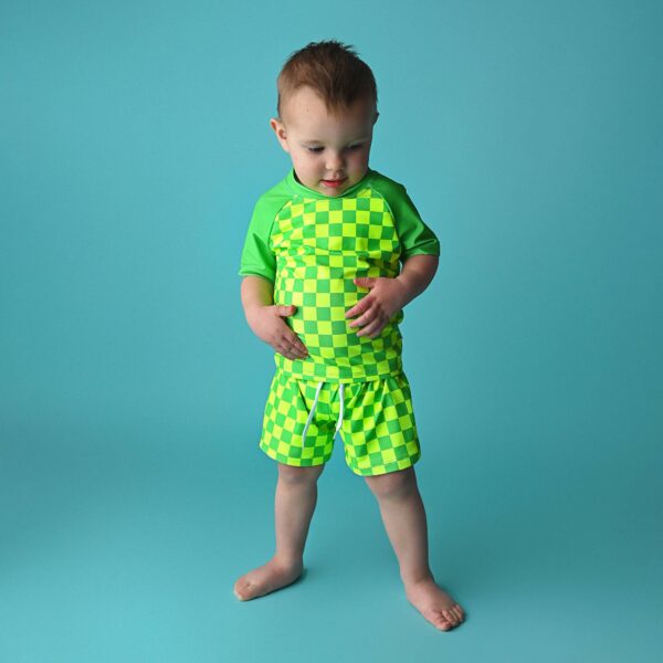 gigi and max brad green neon swim set Toddler in green checkered outfit on blue background.