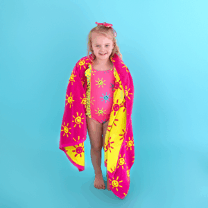 Smiling girl in swimsuit with sun-pattern towel.