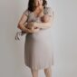 Smiling woman holding newborn in beige dress.