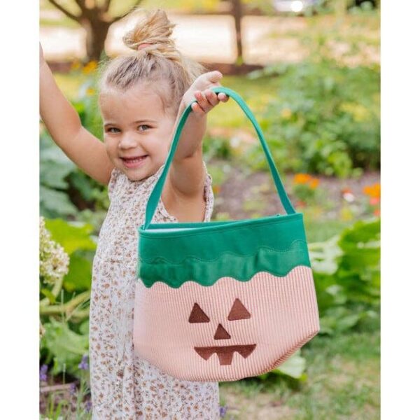 bits & bows jack o lantern pumpkin tote Child holding Halloween-themed basket outdoors.