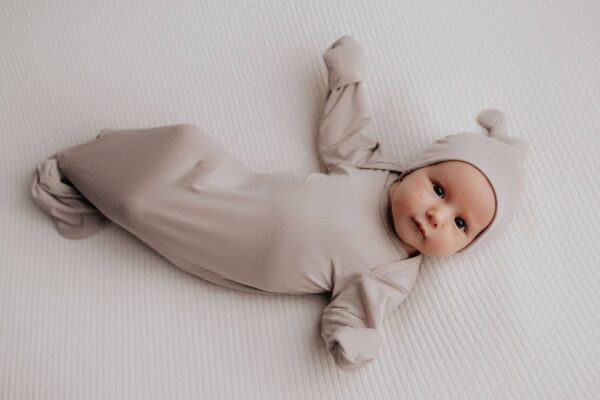 three little tots harbor mist taupe knotted gown Baby in beige outfit lying on bed