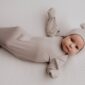 Baby in beige outfit lying on bed
