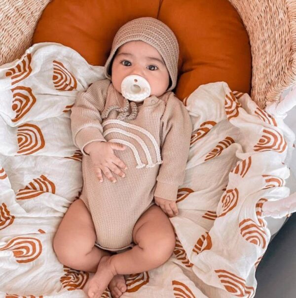 itzy ritzy sweetie soother™ pacifier sets (2 pack): agave + succulent cables Baby in beige outfit with pacifier, cozy bedding.