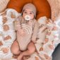 Baby in beige outfit with pacifier, cozy bedding.