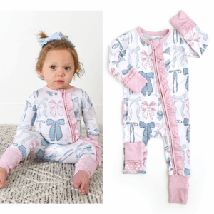 Baby wearing bow-patterned romper on patterned rug.