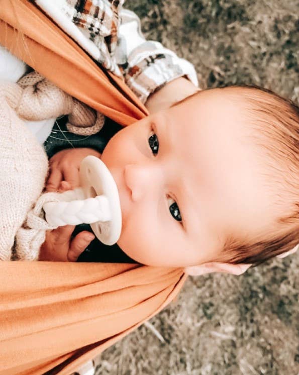itzy ritzy sweetie soother™ pacifier sets (2 pack): toast + buttercream braids Baby in sling with pacifier, eyes open