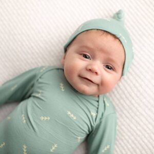 Smiling baby in green outfit on white blanket.