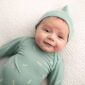 Smiling baby in green outfit on white blanket.