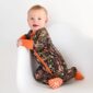 Baby in camo onesie on white chair smiling