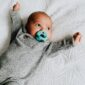 Baby with pacifier lying on patterned blanket.
