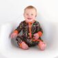 Smiling baby in camo onesie sitting on chair.