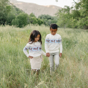 Children walking hand in hand through grassy field.