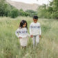 Children walking hand in hand through grassy field.