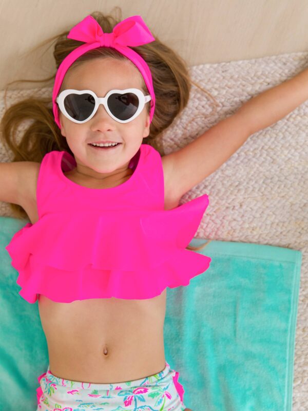 rufflebutts + ruggedbutts girls tropical resort flounce bikini Girl in pink swimsuit and heart-shaped sunglasses