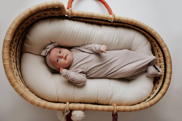 three little tots harbor mist taupe knotted gown Baby in a cozy wicker bassinet.