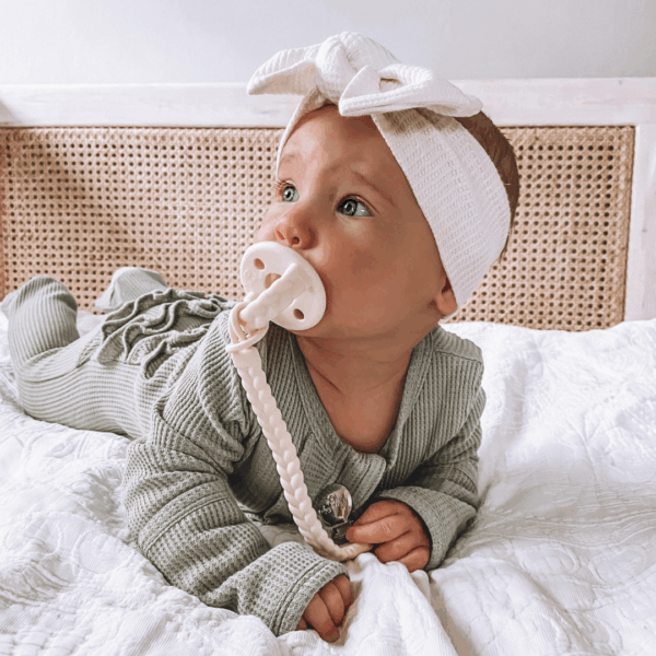 itzy ritzy sweetie soother™ pacifier sets (2 pack): agave + succulent cables Baby with pacifier lying on a bed.