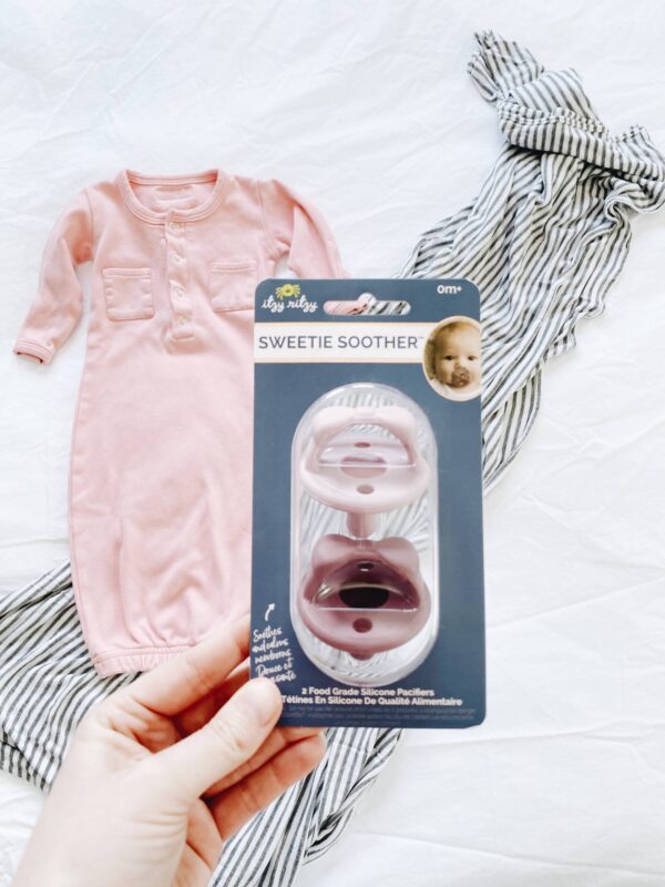 itzy ritzy sweetie soother™ pacifier sets (2 pack): agave + succulent cables Pink baby gown and pacifier set on display.