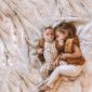 Two children cuddling on a soft, beige blanket.