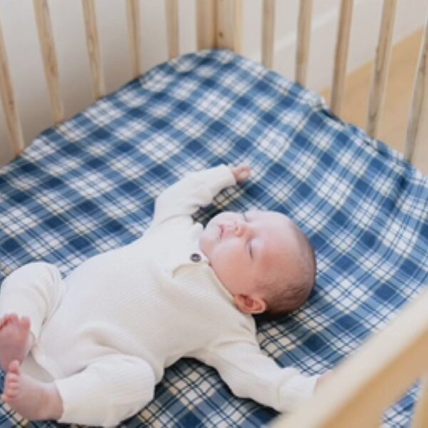 Sleeping baby in crib with plaid blanket.
