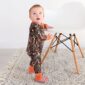 Baby in camouflage onesie stands by chair.