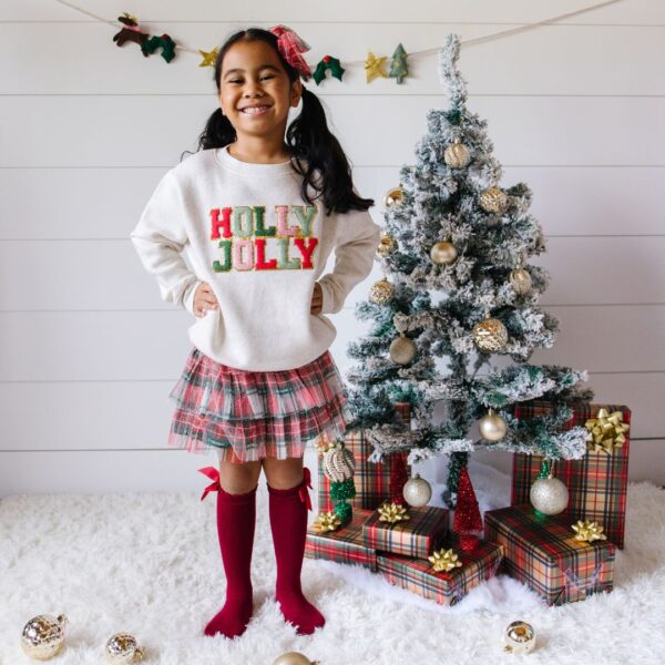 sweet wink christmas plaid tutu Child smiling near Christmas tree with gifts.