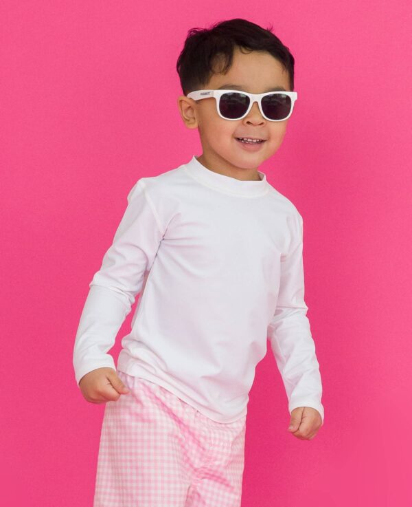 rufflebutts white long sleeve rash guard Child wearing sunglasses against pink background