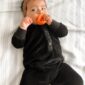 Baby chewing toy on bed in black outfit.