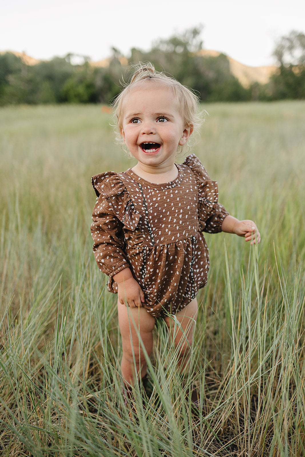 Smiling toddler in brown outfit in grassy field.