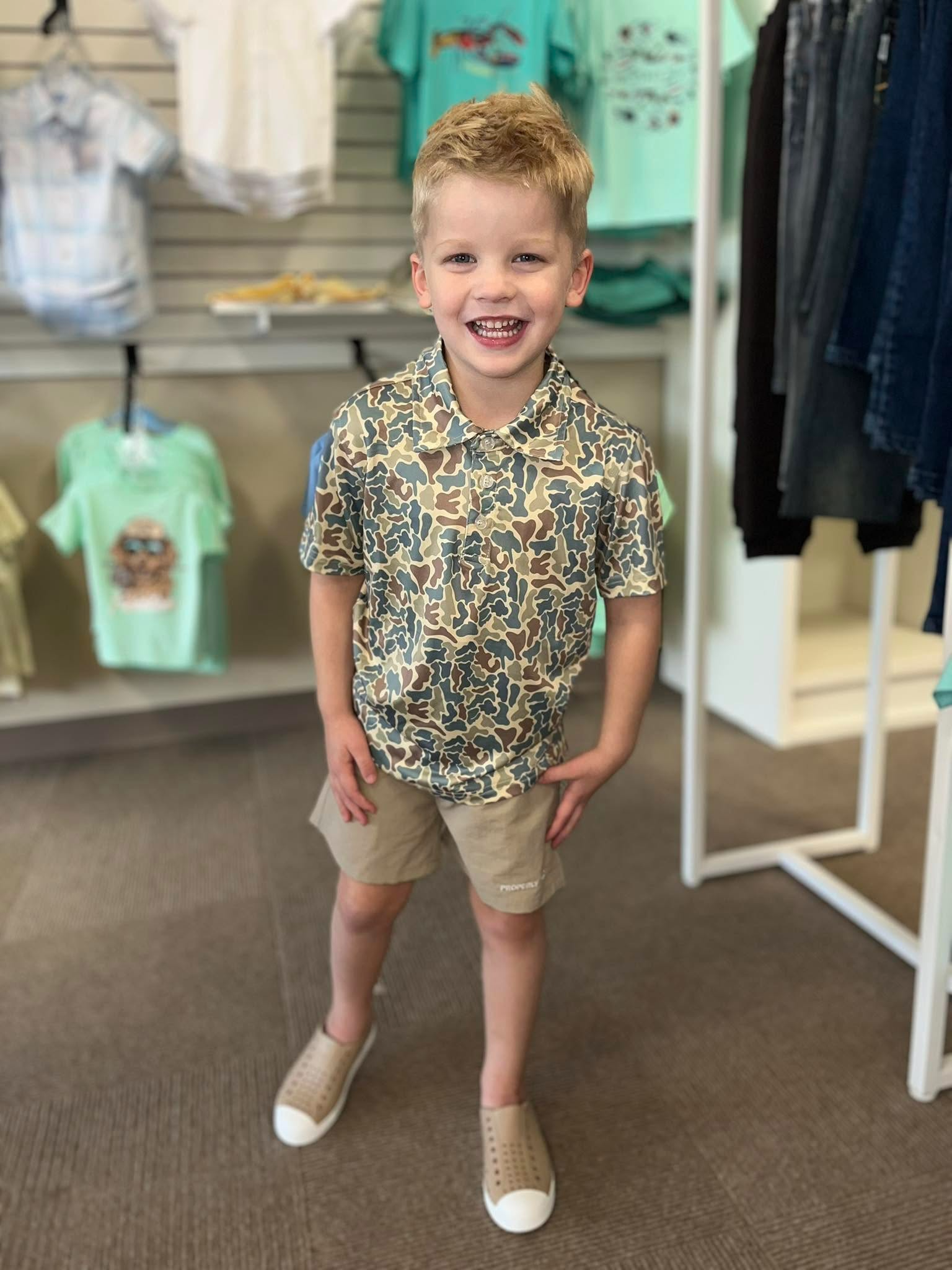 Smiling child in patterned shirt and khaki shorts.