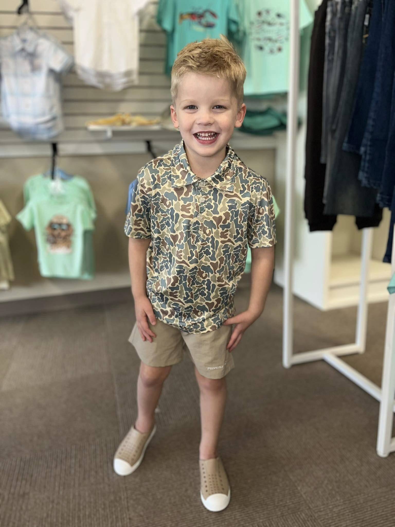 Smiling child in camouflage shirt at clothing store.