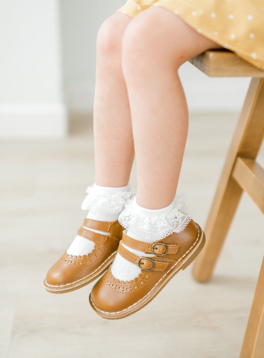 Child wearing brown leather shoes with lace socks.
