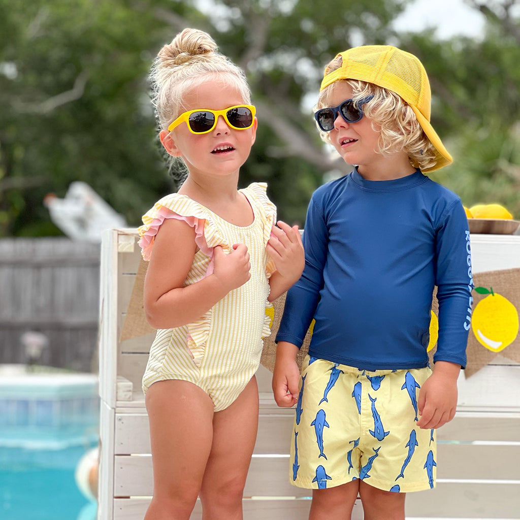 Kids in swimsuits by pool with sunglasses.